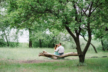 happy guy in a white shirt and a girl in a turquoise dress are walking in the forest park