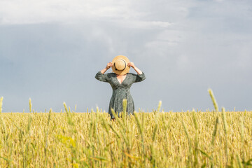 Woman in straw hat walking through the rye field on summer day. Hiding face behind her round hat.