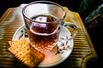 Creative Close-up Photography of A Cup of Hot Tea On The Small Textured Table. Red, black tea in a transparent glass mug served with biscuit on a plate. Herbal Green Tea With Breakfast In The Morning.