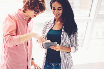 Two male and female classmates watching streaming video in social networks enjoying leisure time together during break using modern touchpad and fast 5G wireless connection in university wifi zone
