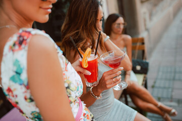 Three beautiful young caucasian women in short summer dresses are sitting and drinking cocktails in the cafe garden. Girls at parties