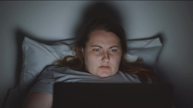 Young fat woman using laptop computer in bed at night time