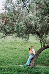 happy guy in a white shirt and a girl in a turquoise dress are walking in the forest park