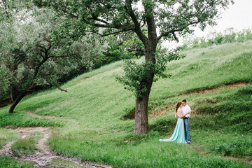 happy guy in a white shirt and a girl in a turquoise dress are walking in the forest park