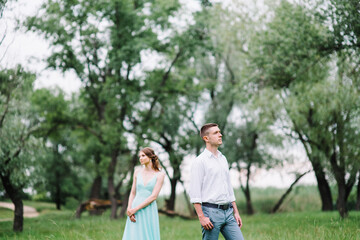 Naklejka na ściany i meble happy guy in a white shirt and a girl in a turquoise dress are walking in the forest park