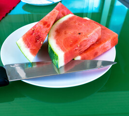 Slices of red ripe sweet watermelon on a white plate on the green glass table