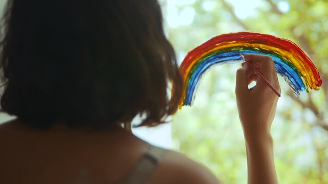 kid girl at home on the window draws a rainbow during coronavirus Covid-19 the quarantine period on self-isolation. Stay at home social media share. daughter child pandemic creative lifestlye