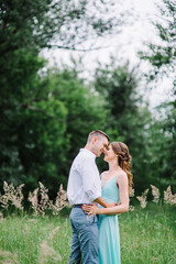 happy guy in a white shirt and a girl in a turquoise dress are walking in the forest park