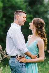 happy guy in a white shirt and a girl in a turquoise dress are walking in the forest park