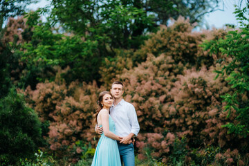 happy guy in a white shirt and a girl in a turquoise dress are walking in the forest park