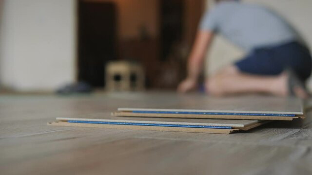 Close-up a stack of laminate is lying on the floor in the apartment, the master takes a bar of laminate and puts it on the floor.