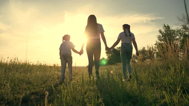 Happy family.A young mother walks with her children in a field at sunset. Two cute girls hold the hand of their mother, sister, teacher