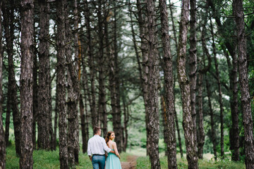 Obraz premium happy guy in a white shirt and a girl in a turquoise dress are walking in the forest park