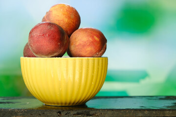 Fresh peaches in bowl on natural green background.