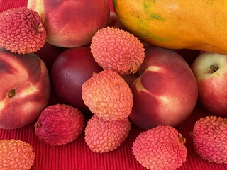 Mix fruit: fresh red peaches, nectarine. mango and lychee on red cloth napkin