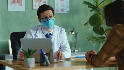 Professional doctor consulting with woman patient in the hospital, giving instructions and using...