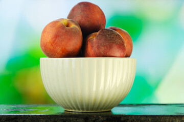 Ripe red peaches in bowl on natural green background.