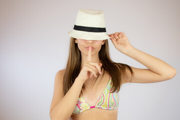 Girl in bikini with hat making the silence gesture