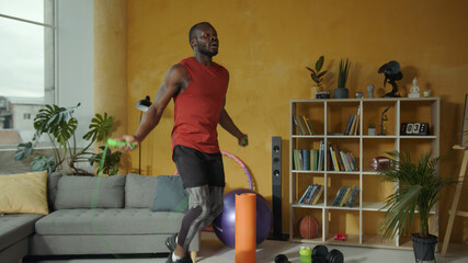 Energetic young african american athlete jumps on rope performing active cardio exercises workout cross fit training at home. © Fractal Pictures