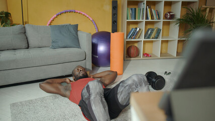 African american athlete performing abdominal core crunches on floor while watching online classes training. Home fitness. Workout. Self-isolation during quarantine.