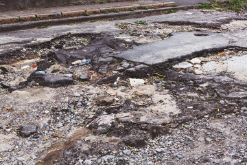 A road damaged by rain and snow, that is in need of maintenance. Broken asphalt pavement resulting in a pothole, dangerous to vehicles.