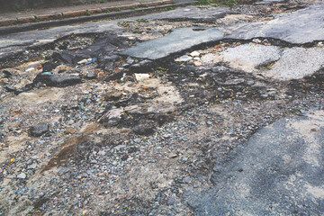 A road damaged by rain and snow, that is in need of maintenance. Broken asphalt pavement resulting in a pothole, dangerous to vehicles.