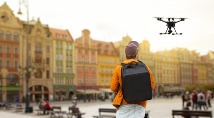 A man with a backpack controls a drone on a background of a European city