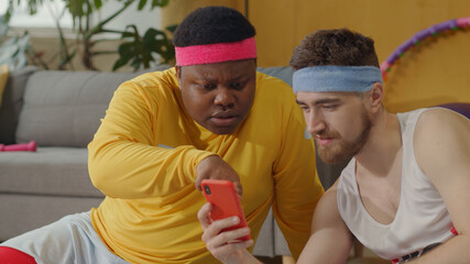 Team of friendly diverse retro style men using smartphone, watching online coaching training classes on mobile phone social media in the living room.
