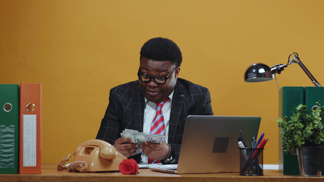 Satisfied african employee receives bunch of money on payday. Handsome happy black businessman counts money banknotes working at modern office corporation.