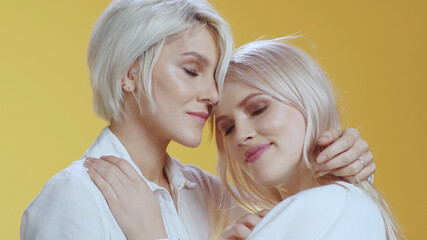 Beauty tender blonde girls of LGBT lesbian couple family embracing each other feel much happy kissing and smiling together on background. Copy space.