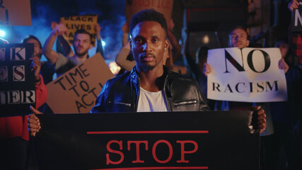 Portrait black young man activist with Stop Racism banner protesting violence in multi-ethnic...