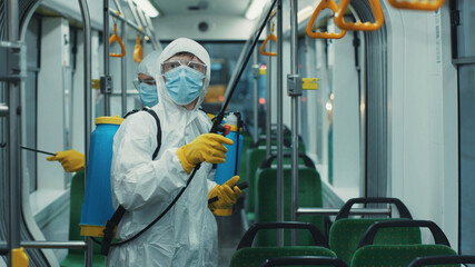 Team of janitors doing antibacterial cleaning of public transport. Two male cleaners disinfecting tram from coronavirus infection. Health care. Pandemic.