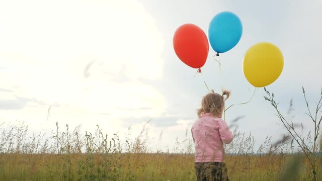 daughter little girl fun runs with balloons a on her birthday outdoors by field. dream happy family concept. child girl kid lifestyle day. child is running and balloons on a background of blue sky