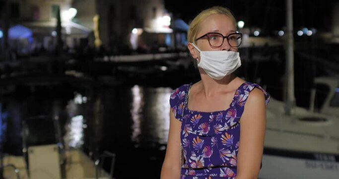 Evening shot of a young woman on a pier wearing a face mask in the wrong way. The concept of maintaining social distance and the corona virus pandemic.
