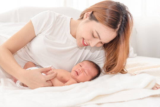 Close up portrait of beautiful young asian mother with newborn baby. Side view of a young woman playing with her little baby in bed.