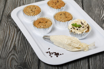 Banana cupcake. With butter cream and banana jam. Decorated with mint leaves and chocolate sprinkles. Next to them are cupcakes without cream and a pastry bag with cream.