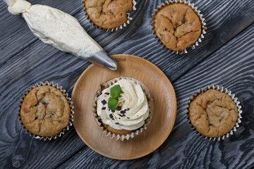 Banana cupcake. With butter cream and banana jam. Decorated with mint leaves and chocolate sprinkles. Next to them are cupcakes without cream and a pastry bag with cream.