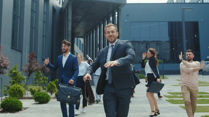 Excited multi-thnic office staff dancing on street after working day. Happy friendly corporate team performing group dance to celebrate success in business.