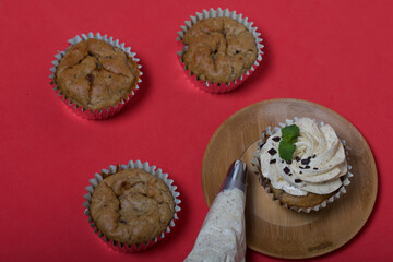 Banana cupcake. With butter cream and banana jam. Decorated with mint leaves and chocolate sprinkles. Next to them are cupcakes without cream and a pastry bag with cream.