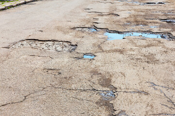 A road damaged by rain and snow, that is in need of maintenance. Broken asphalt pavement resulting...