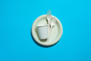 disposable biodegradable fork, spoon, glass and plate of cornstarch on a blue background. environmentally friendly dishes. isolate. replacement of eco plastic with modern bio materials