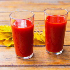 Tomato juice in a glass cup and yellow autumn leaves on a wooden table. Selective focus.