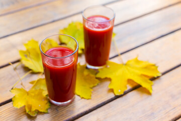 Tomato juice in a glass cup and yellow autumn leaves on a wooden table. Selective focus.