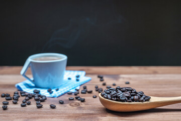 Roasted coffee beans on wood spoon and hot coffee in cup with smoke on the wood floor.