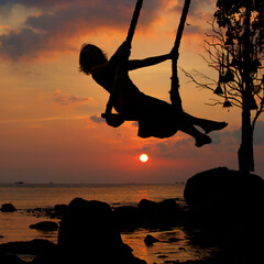 A girl's silhouette on a swing against the sea during sunset in Thailand