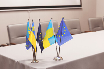 Small flags of the European Union and Ukraine on a white table, a conference hall in the...