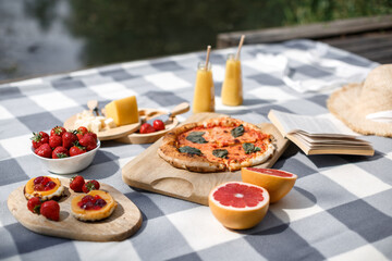 Delicious summer picnic in nature near the lake. Picnic with pizza, sweets, berries and reading books. Outdoor picnic. Focus on food