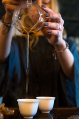 Traditional Chinese Tea Ceremony. Black or Red Tea pouring By a Blonde Caicasian girl into White pial cup on dark Table background
