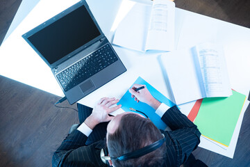 Top view of a businessman with a laptop and documents. The person with headphones is in the office. Telecommuting. Office work. The employee checks the documents.