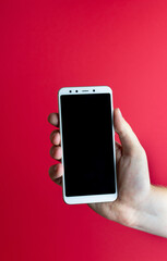 The hand holds the phone against a red background. Mock-up. Copy space.